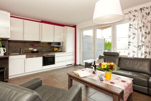 A modern kitchen with white cabinets, a dining area with a table and chairs, and a sofa. - Holiday home with 4 bedrooms (Zinnowitz)