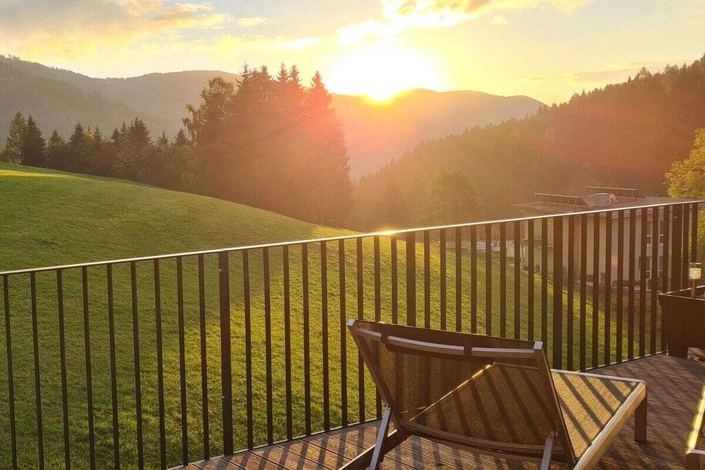 Un balcon donnant sur un champ verdoyant et des montagnes, avec une chaise et une table.