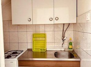 A kitchen with white cabinets, a gas stove, a sink, and a yellow colander. - Apartments Adriana Studio Apartment 6 (Gradac)