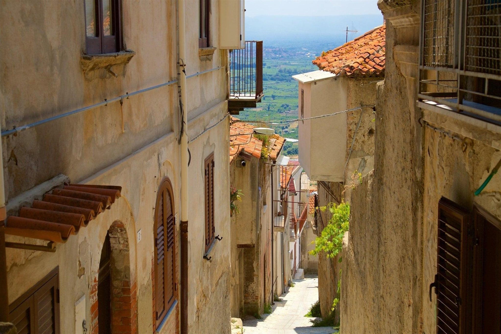 Una stretta via fiancheggiata da edifici, con un balcone ben visibile e vista sulla campagna.