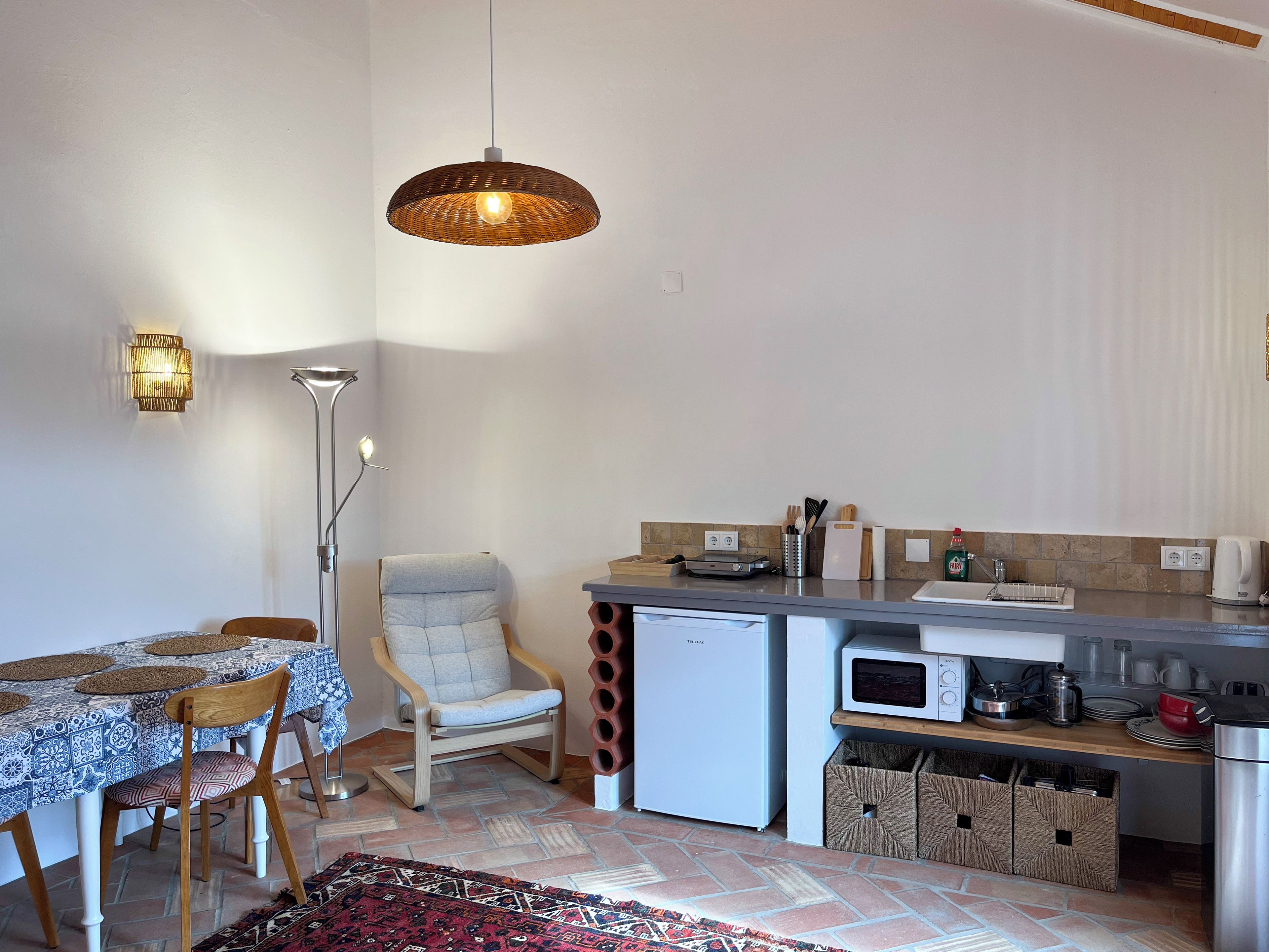 Cozinha compacta com área de refeições, micro-ondas, geladeira e luminária pendente.