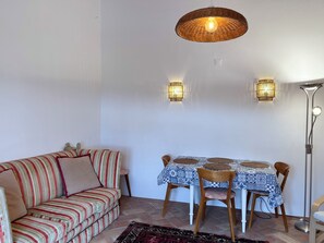 Una habitació amb un sofà a ratlles, una taula de dinar amb mantell estampat i dues làmpades penjades a la paret.