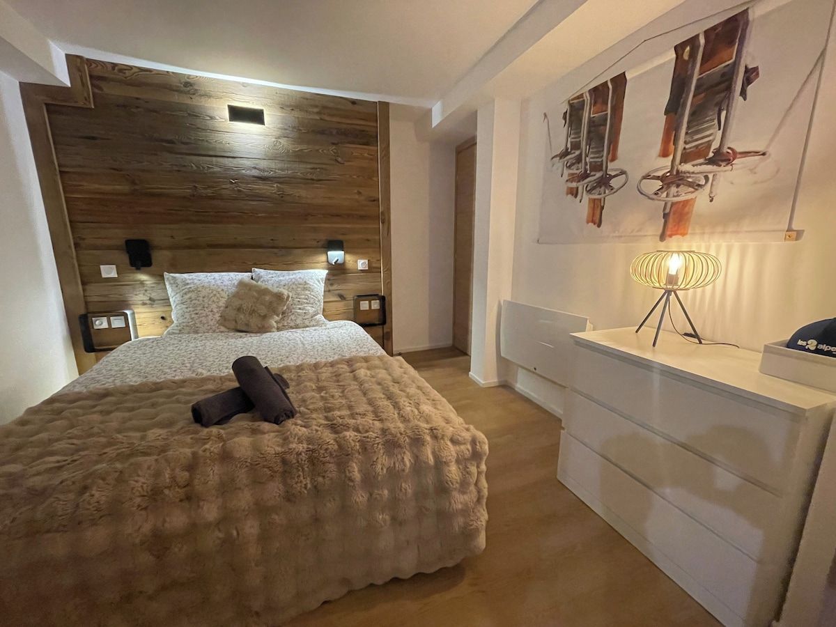Ein Schlafzimmer mit Holz-Kopfteil, einem Bett mit flauschiger Decke, einem Nachttisch mit Lampe und einer Kommode mit Schubladen.