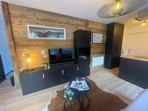 Ein modernes Wohnzimmer mit einer Wandpaneinung aus Holz, einer schwarzen Unterhaltungseinheit, einem runden Couchtisch mit Zeitschriften und einem Kuhfellteppich.