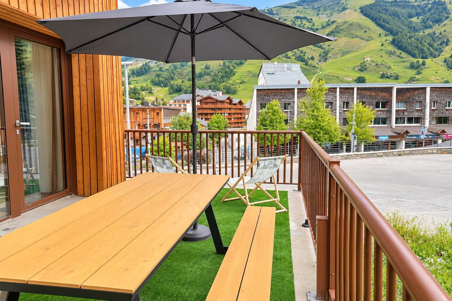 A wooden deck with a table and chairs, a large umbrella, and a view of buildings and hills in the background.