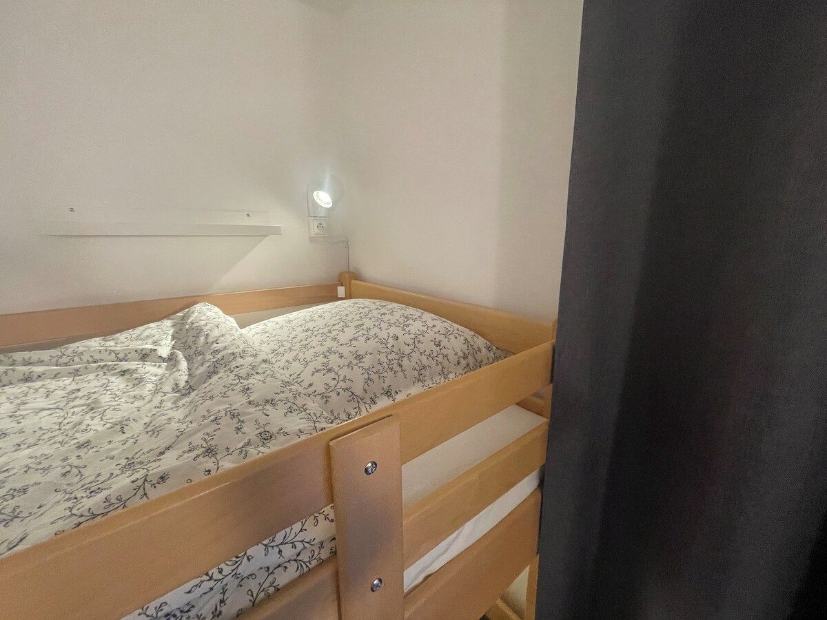 A single bed with a floral-patterned mattress, a bedside table with a drawer, and a wall-mounted light fixture.