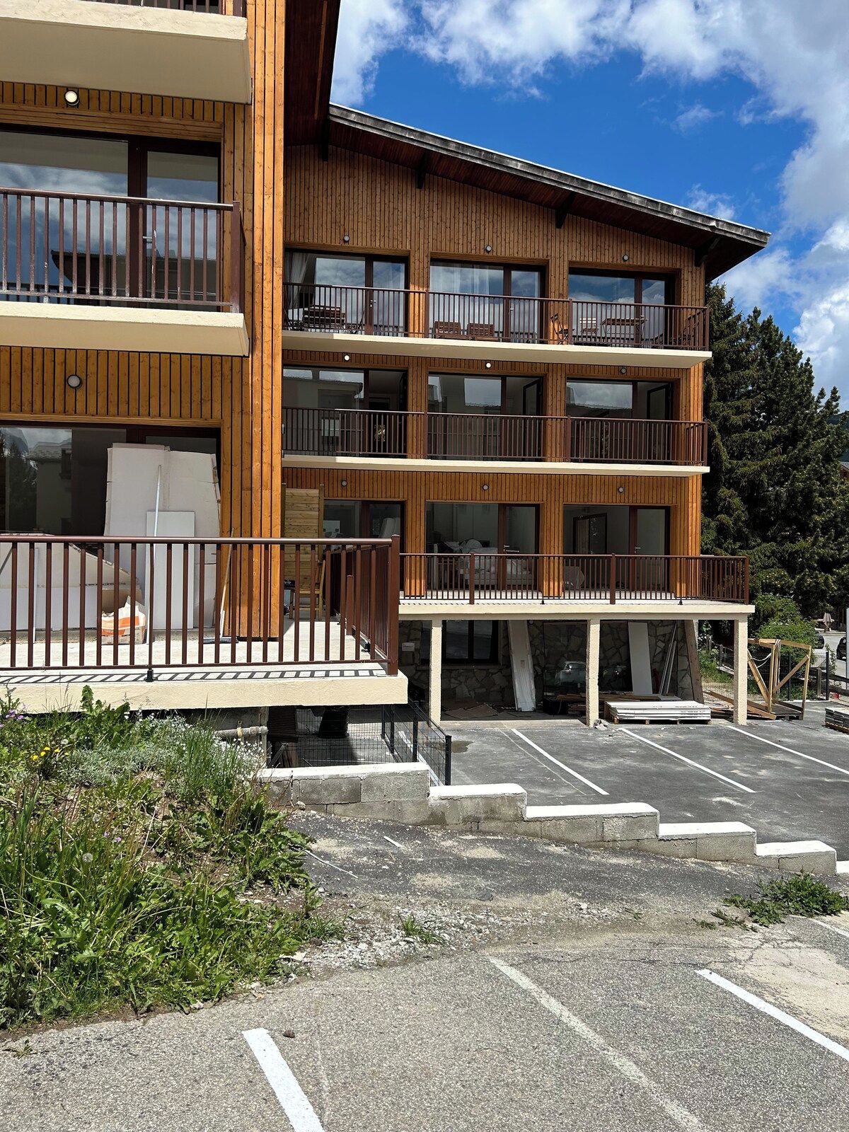 A multi-story wooden building with balconies, a covered entrance, and a parking area.