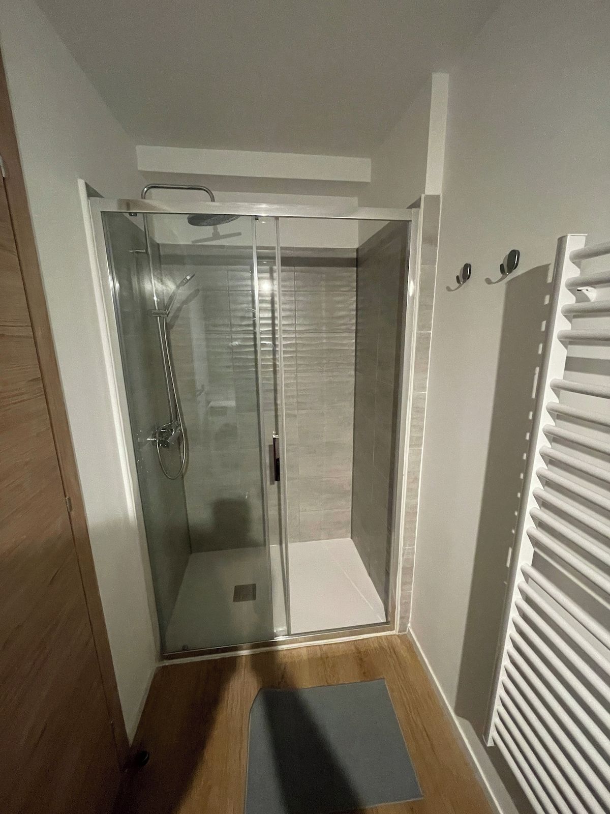 A glass-enclosed shower room with a wooden floor and a white ceiling.