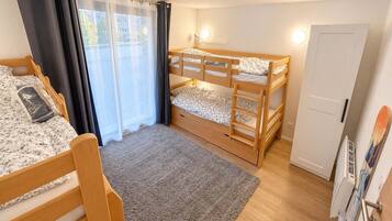 A room with two bunk beds, a window with curtains, a door, and a small rug.