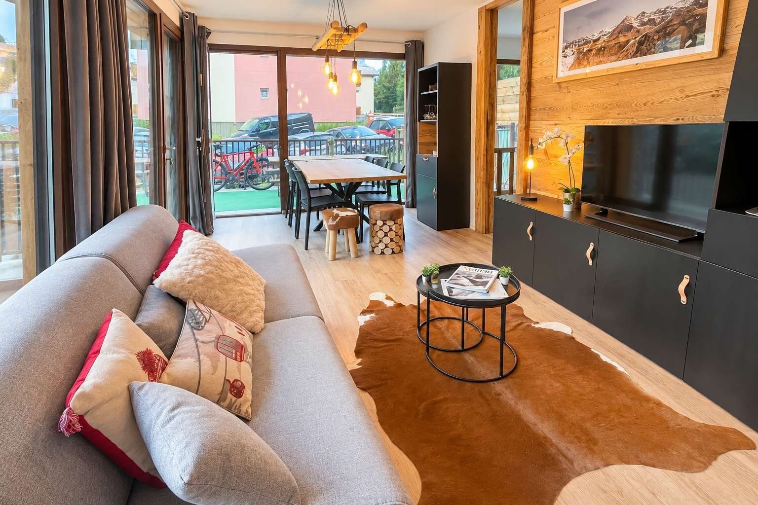 A modern living room with a sofa, a coffee table, and a TV. There is a dining area with chairs and a table.