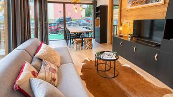 A modern living room with a sofa, a coffee table, and a TV. There is a dining area with chairs and a table.