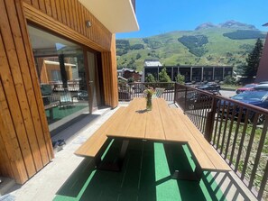 Eine Holzterrasse mit Tisch und Stühlen, eine Glastür und Blick auf eine Berglandschaft.