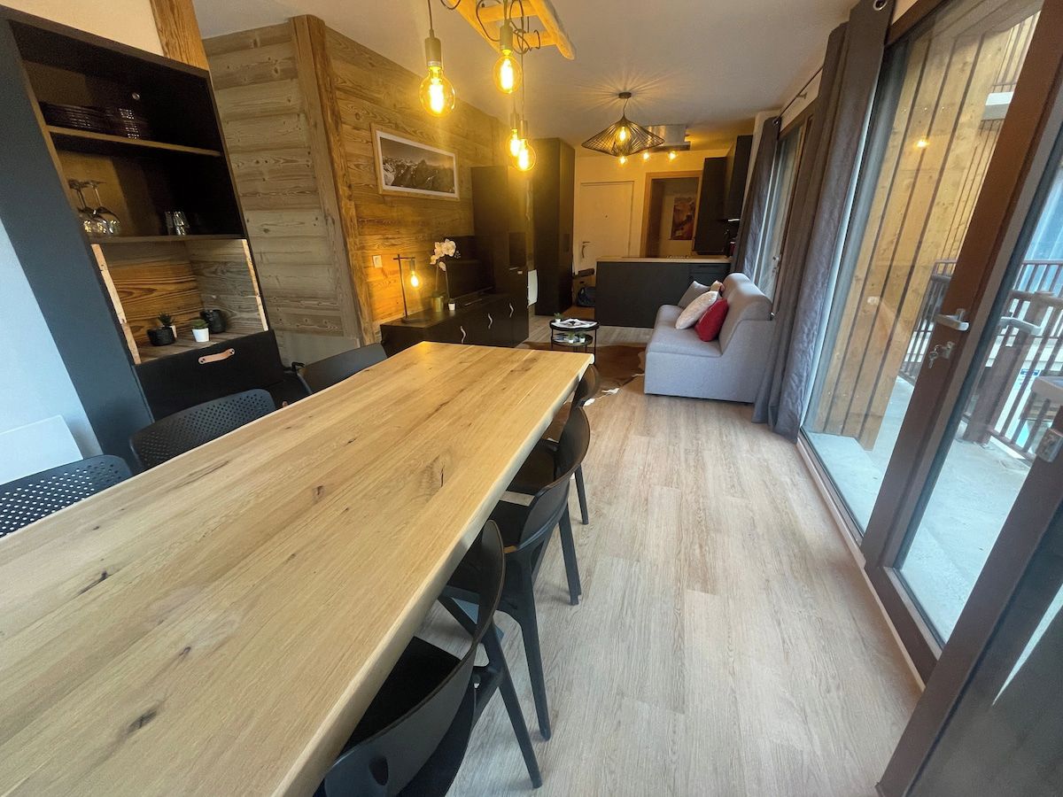 A modern kitchen with a wooden table, black chairs, and pendant lighting.