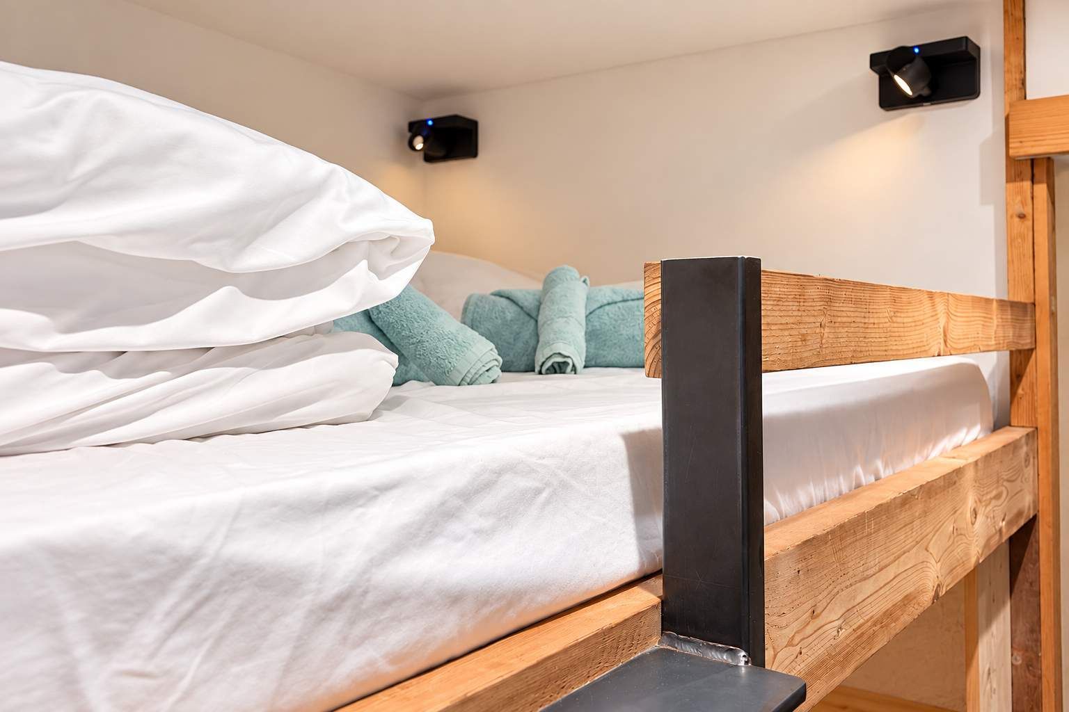 Un lit superposé avec une literie blanche, une tête de lit en bois et deux lampes de lecture fixées au mur.