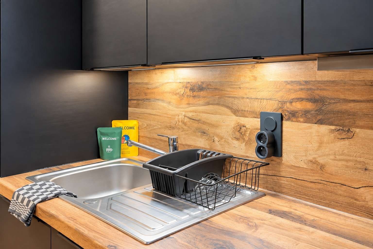 Een moderne keuken met een roestvrijstalen spoelbak, een afwasschaal en een houten achterwand.