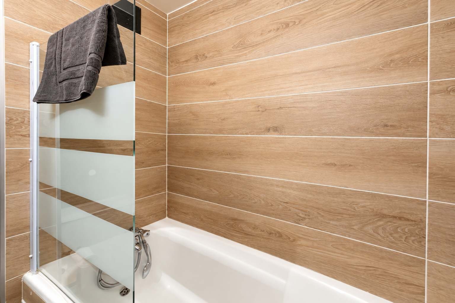 Un baño moderno con cabina de ducha de vidrio, una bañera blanca y revestimiento de madera en las paredes.