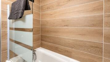 Un baño moderno con cabina de ducha de vidrio, una bañera blanca y revestimiento de madera en las paredes.