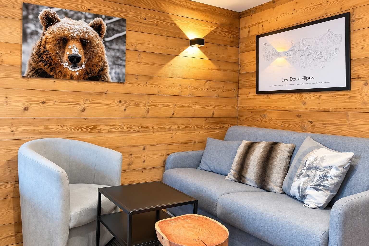 Quarto acolhedor com parede de madeira, sofá azul claro, poltrona combinando, uma pequena mesa e uma imagem de um urso.