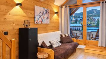 Interior acollidor d'una cabana amb elements de fusta, un sofà amb coixins, una taula petita, un objecte decoratiu a la paret i vista a un paisatge de muntanya a través d'una finestra gran.