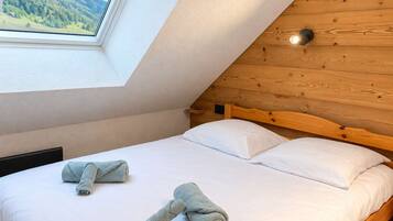 A bedroom with a sloped ceiling, a wooden headboard, and a window with a view of a forest.