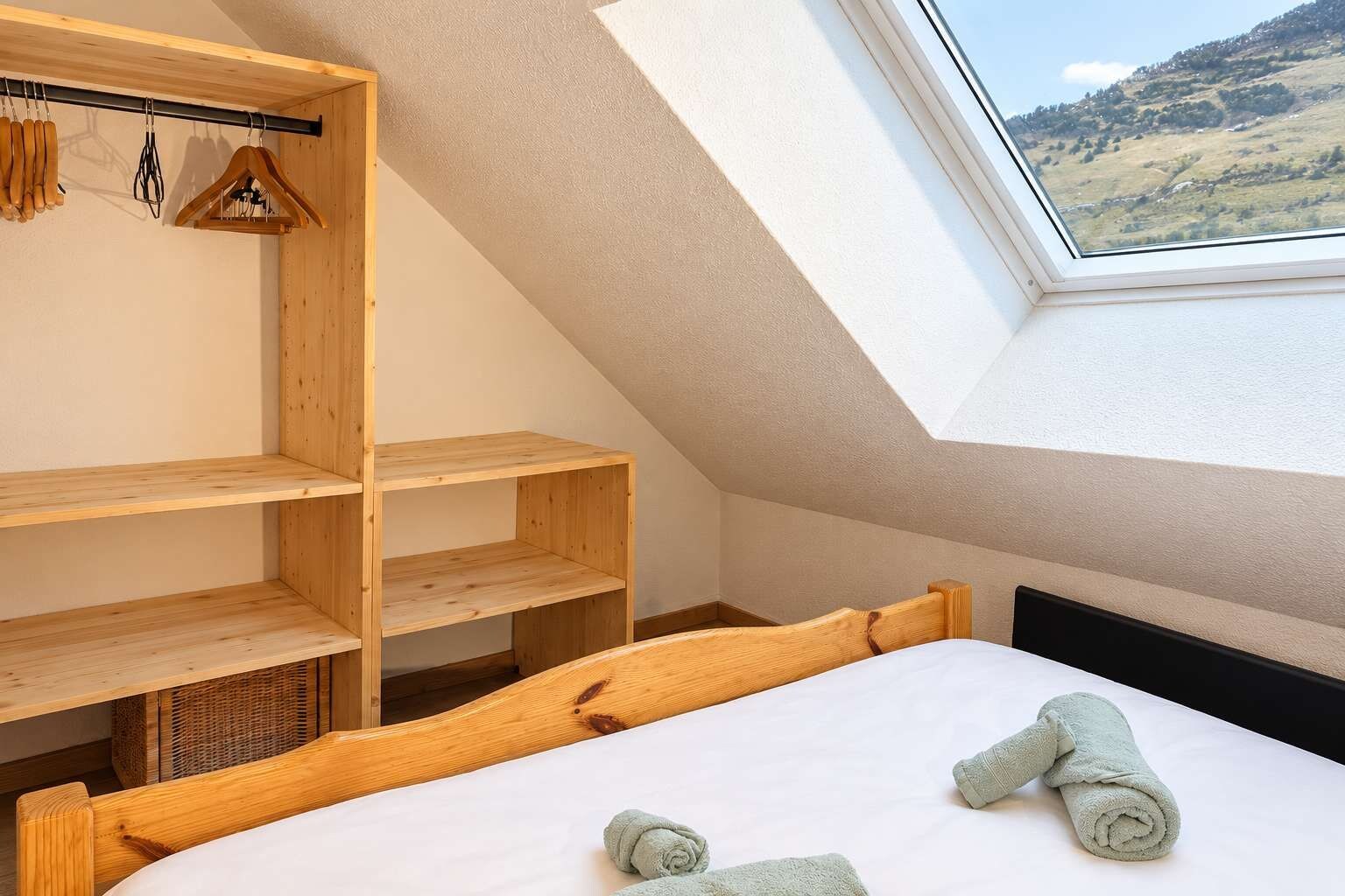 Ein Schlafzimmer mit schrägen Wänden, einem Holzkopfende und einem Oberlicht.