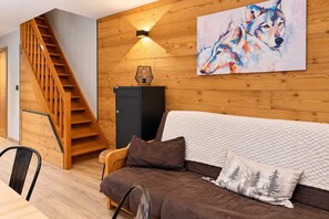 Ein modernes Wohnzimmer mit einer Holztreppe, einer Couch mit Kissen, einem Wolfsbild und einer Wandlampe.