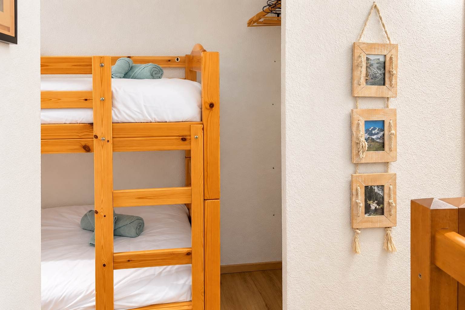 Un lit superposé avec une structure en bois et une literie blanche, un cadre photo fixé au mur contenant trois photos, et une chaise en bois.