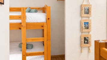 Un lit superposé avec une structure en bois et une literie blanche, un cadre photo fixé au mur contenant trois photos, et une chaise en bois.