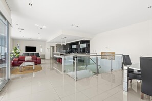 A modern living space with a red sofa, a glass partition, and a kitchen area. - Ocean 100 ~ Aldinga Beach - Ultimate Beachfront Family Escape (Aldinga Beach)
