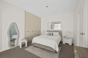 A bedroom with a bed, a nightstand, a mirror, a wardrobe, and a small stool. - Ocean 100 ~ Aldinga Beach - Ultimate Beachfront Family Escape (Aldinga Beach)