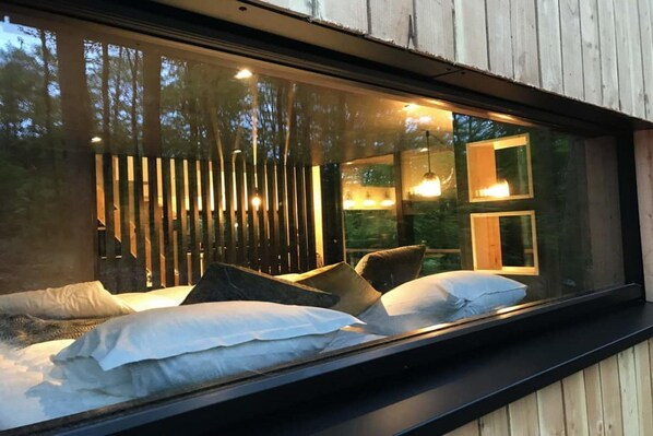 Ein Schlafzimmer mit einem Bett, Kissen und einem Fenster mit Blick auf einen Wald.