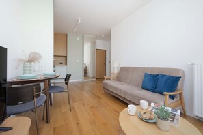 Ein modernes Wohnzimmer mit Sofa, Esstisch, Stühlen und einer Küchenzeile im Hintergrund.