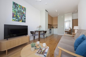 Ein modernes Wohnzimmer mit einem Flachbildfernseher, einer Couch, einem Couchtisch mit einer Zeitschrift und einem Essbereich mit Stühlen und einem Tisch.