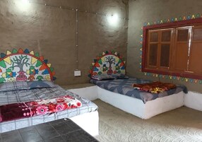 Una habitación con dos camas, una con colcha estampada floral y otra con diseño geométrico. Se ve una ventana con marco de madera y una pared decorada con patrones geométricos coloridos.