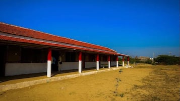 Un edificio con techo rojo y pilares blancos, un área exterior cubierta y cielo despejado.
