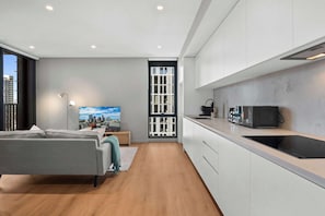A modern apartment with a kitchenette, a bed, a cityscape view, and a large window. - High-Rise 2-Bed Apartment Near South Melbourne (South Melbourne)