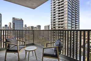 Ein Balkon mit zwei Stühlen und einem kleinen Tisch, mit Blick auf eine Stadtlandschaft mit Hochhäusern.