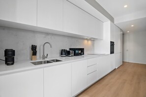 Eine moderne Küche mit weißen Schränken, einer Spüle aus Edelstahl, einer Kaffeemaschine, einem Toaster und einer Mikrowelle.