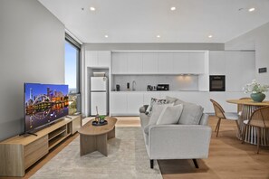 Ein modernes Wohnzimmer mit Flachbildfernseher, grauem Sofa, Couchtisch und Essbereich mit rundem Tisch und Stühlen.