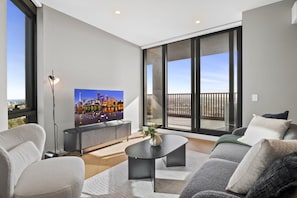 Ein modernes Wohnzimmer mit Flachbildfernseher, einer Couch, einem Couchtisch und einem Balkon mit Blick auf die Stadt.