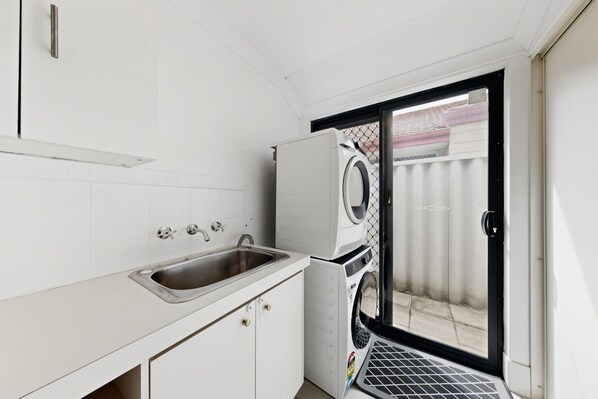 A compact laundry room with a washing machine, a sink, and a door leading outside.