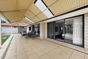 A covered patio area with a table and chairs, a brick wall, and a sliding glass door leading to an interior room.