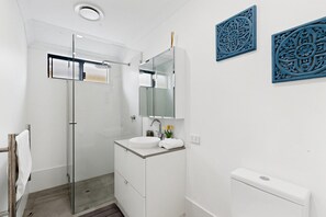 A modern bathroom with a glass shower enclosure, a white sink, and a toilet. - Spacious 4-Bed House Near Mandurah (Dudley Park)