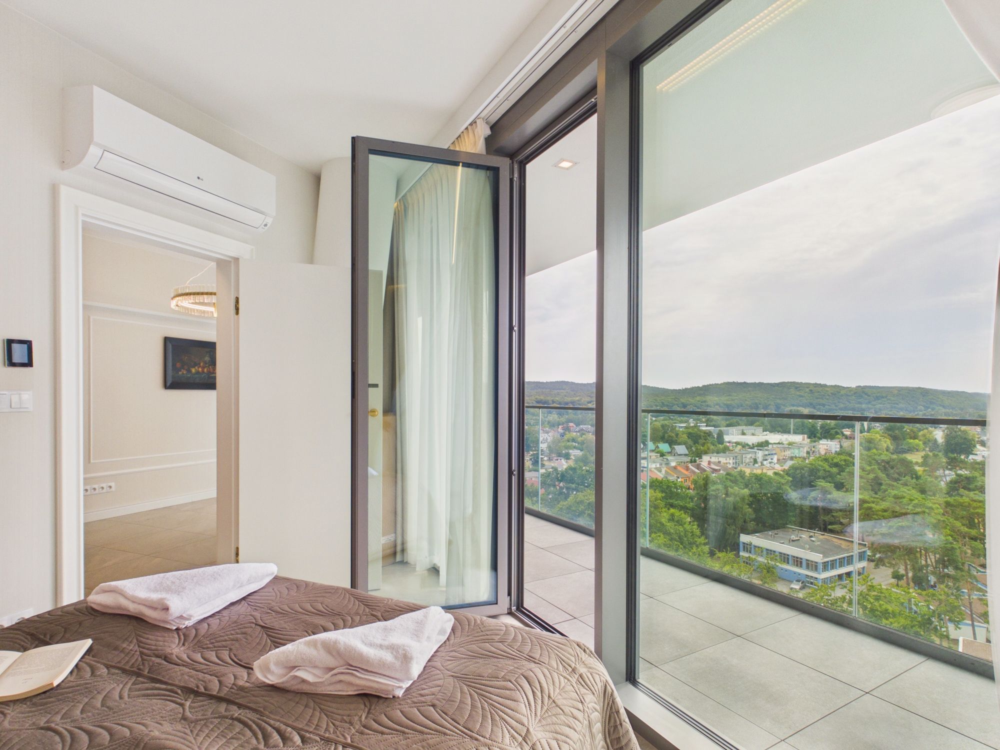Une chambre d’hôtel avec une grande fenêtre, un lit recouvert d’une courtepointe, une porte et une vue sur le paysage urbain.