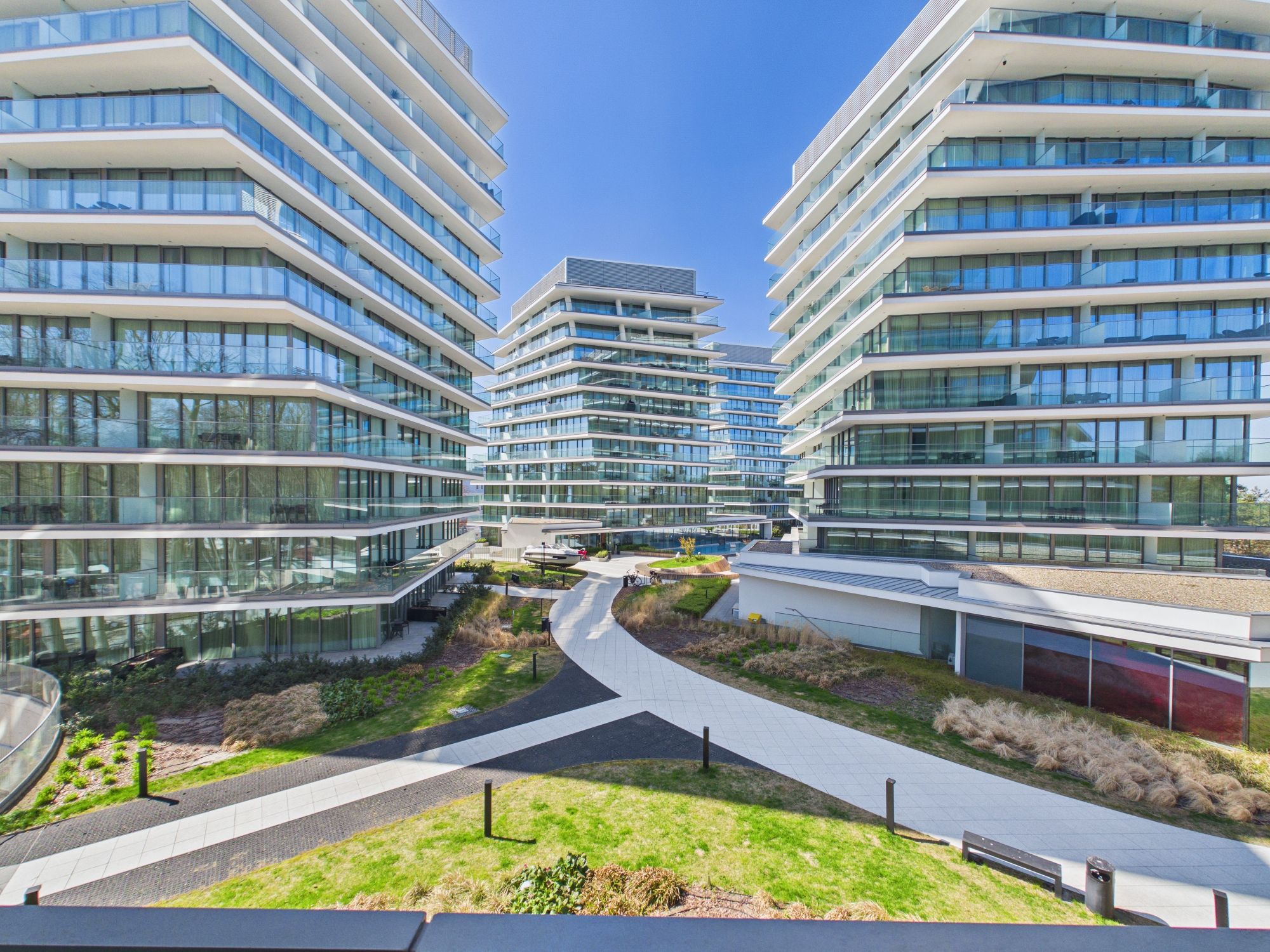 Un bâtiment moderne à plusieurs étages, doté d’une façade en verre, d’une cour intérieure et d’un chemin sinueux.