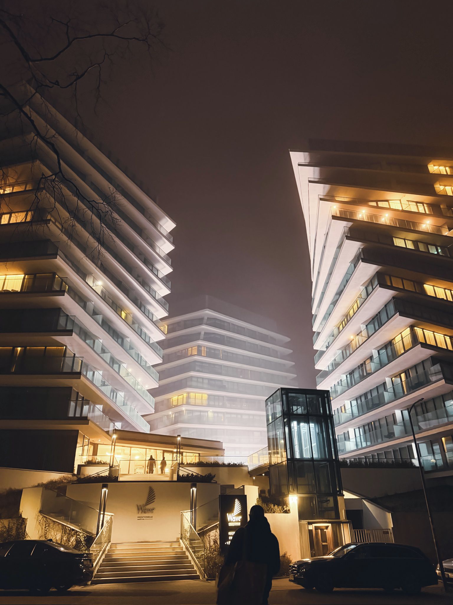 Un bâtiment moderne à plusieurs étages, doté de balcons et d’une entrée centrale surélevée par des marches.