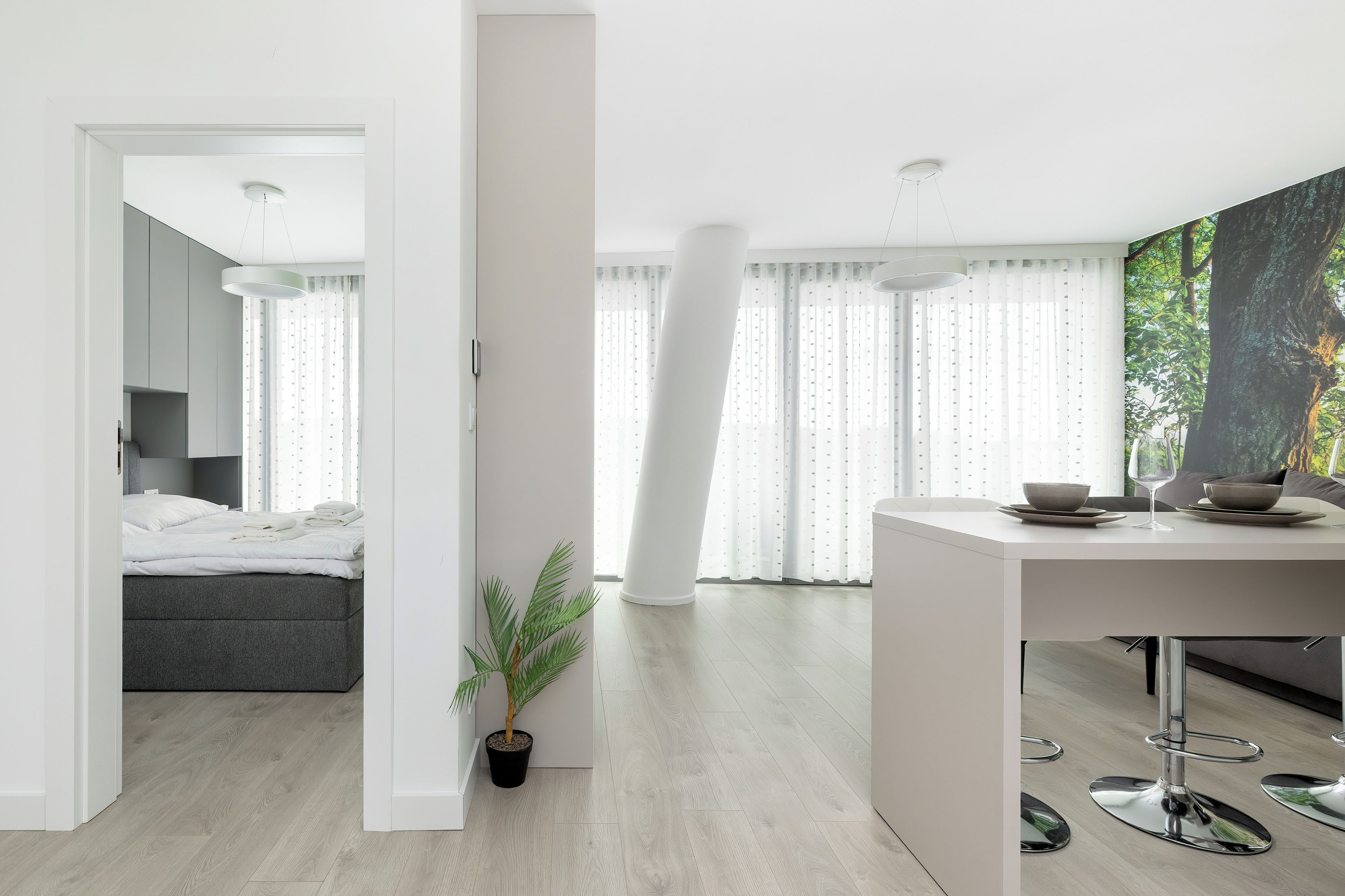 A modern interior with a bed, a dining area, and a large window with curtains.