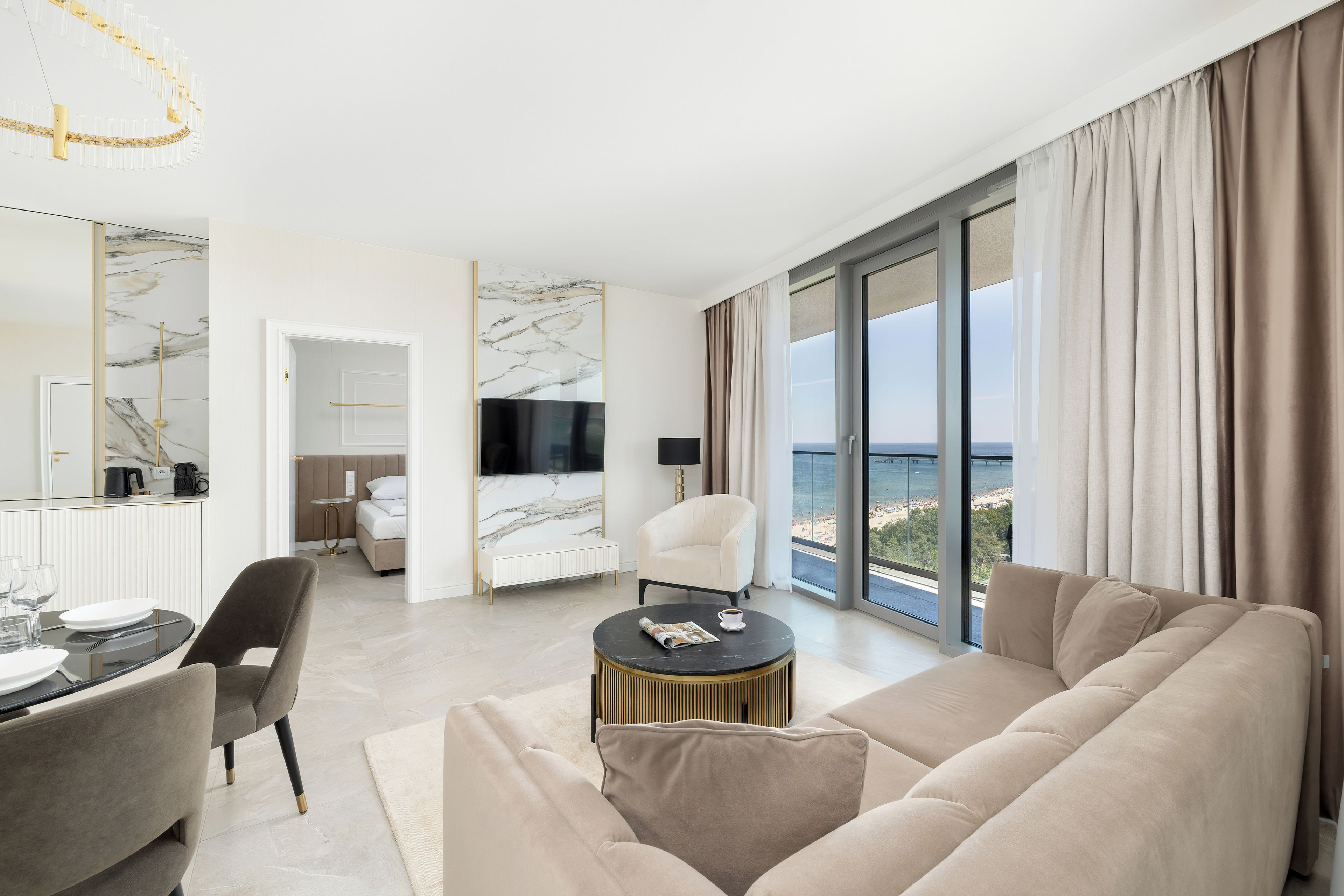 Une chambre d’hôtel moderne dotée d’un grand canapé, d’un coin repas, d’une télévision et d’un balcon offrant une vue sur la mer.