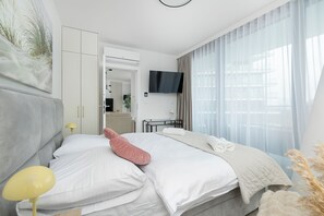 A modern bedroom with a bed, bedside lamp, and a TV mounted on the wall. - Wave Apartments by Solarento (Międzyzdroje)