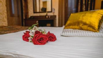 Una cama con sábana blanca, almohada dorada y un ramo de rosas rojas.
